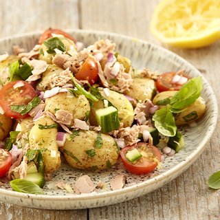 A plate of tuna, vegetable and potato salad, with a squeezed lemon at the side