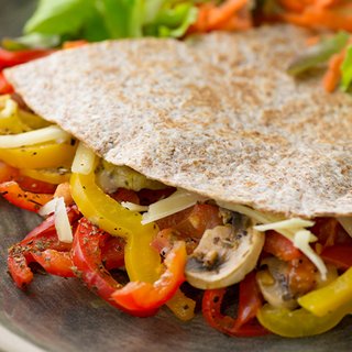 Two "cheats' pizzas" on a chopping board: cooked veg, including mushrooms, peppers and cheese in a folded tortilla