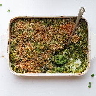 A casserole dish of macaroni with a green cheese sauce and florets of broccoli mixed through