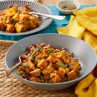 Chunks of fried, curried tofu and sweet potato, served in a bowl with mixed rice and kidney beans.