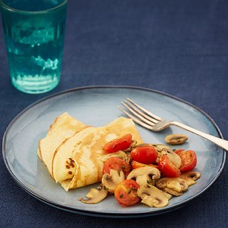 A plate with 2 folded pancakes served with sliced tomatoes and mushrooms