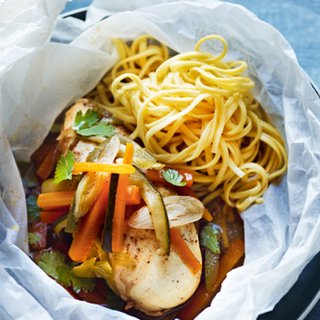 Chicken topped by vegetables in baking parchment, accompanied by noodles
