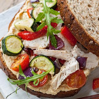A sandwich filled with hummus and a mixture of roasted courgette, aubergine, onion and pepper, and slices of chicken