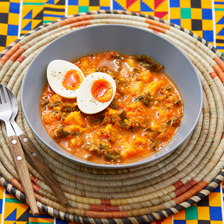 A bowl of mashed potato and sweet potato in a spicy sauce, topped with a halved boiled egg