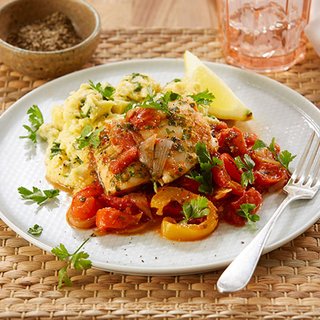 A plate of white fish fillets in tomato, pepper and thyme sauce, with a portion of okra cornmeal and a slice of lemon