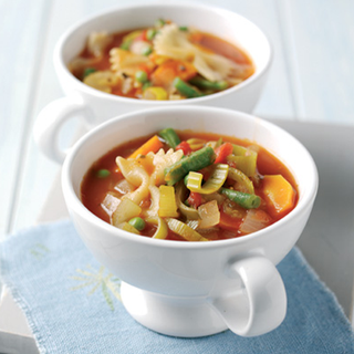 A portion of soup, with pieces of carrot, green bean, celery, tomato and pasta visible