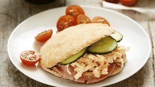 A plate with sliced pitta bread containing ham, coleslaw and cucumbers. Served with cherry tomatoes cut in half.