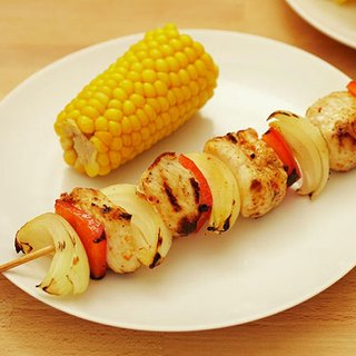 A grilled skewer of chicken, onion and pepper served with a side of corn on the cob