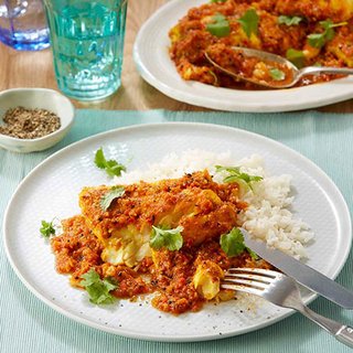 A fillet of fish in a spicy dark orange sauce, served with chopped coriander on a bed of rice