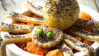 A spider made from pastry with peas as eyes sits on-top of a chicken pie, its legs resting over the bowl.