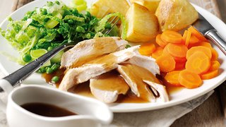 A roast chicken dinner, served with potatoes, carrots, cabbage and gravy.