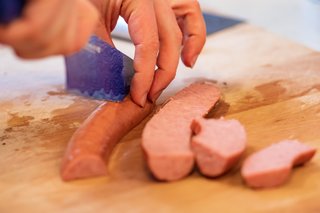 A hot dog cut in half lengthways, then being sliced lengthways into thin strips about 2cm across