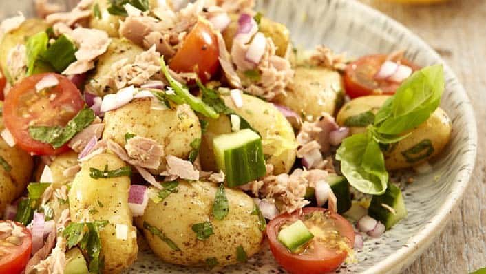A plate of tuna, vegetable and potato salad, with a squeezed lemon at the side