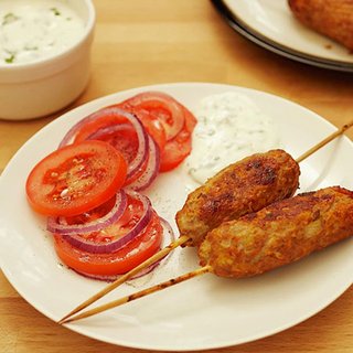 2 homemade turkey koftas, served with tomato and red onion slices, and yoghurt dip