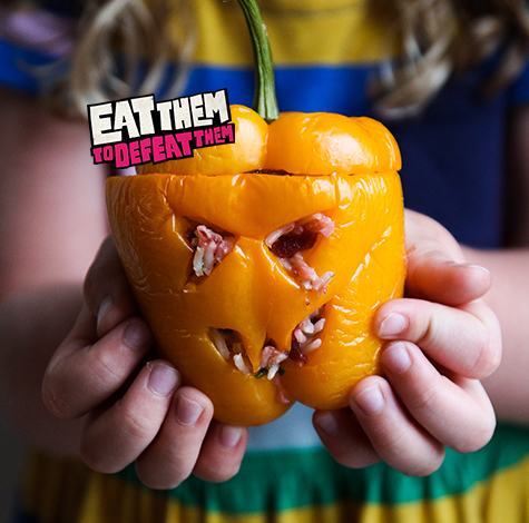 A yellow pepper with a scary face carved into it, stuffed with beetroot-red rice