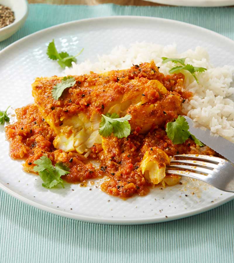 A fillet of fish in a spicy dark orange sauce, served with chopped coriander on a bed of rice