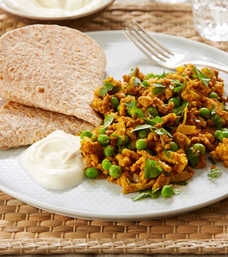 A serving of minced turkey keema, dotted with peas and topped with coriander, on a plate with a chapati and a spoonful of yoghurt