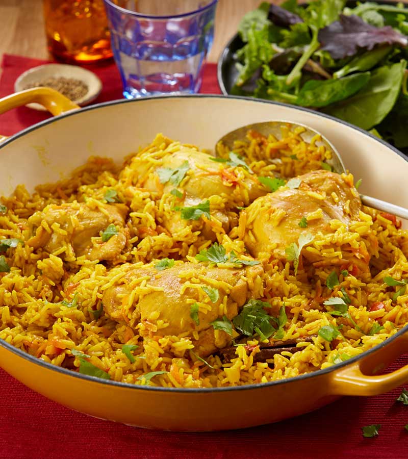 A large pot of spiced rice, chicken, carrot and tomatoes, served with a green salad.