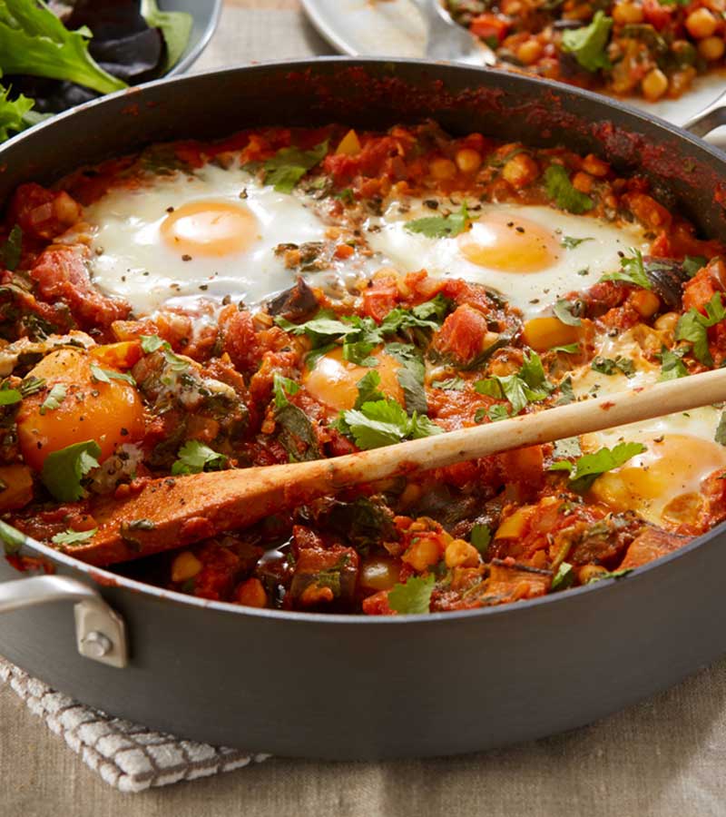 A pan filled with a tomato sauce comprising aubergine, chickpeas and poached eggs, served with pitta.