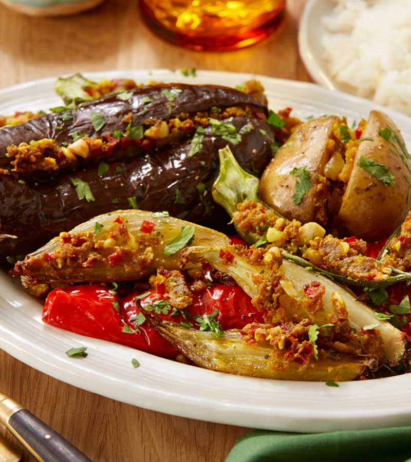 A plate of aubergines, large red peppers, onions and potatoes stuffed with a masala paste mix, served with rice.