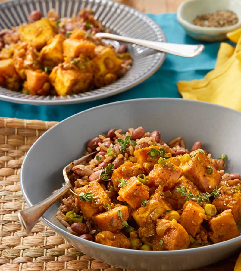 Chunks of fried, curried tofu and sweet potato, served in a bowl with mixed rice and kidney beans.