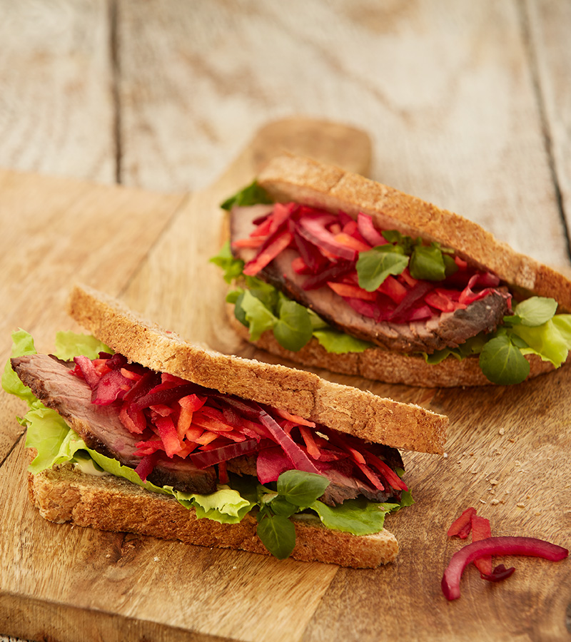 A sandwich cut in half, filled with beef, lettuce, beetroot and red onion, served on a wooden chopping board