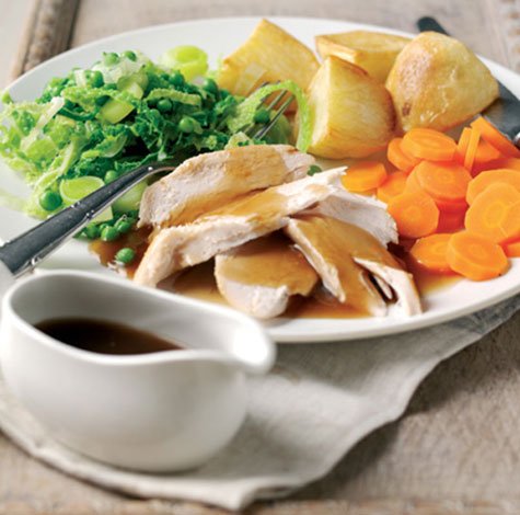 A Sunday roast dinner, with chicken, potatoes, carrots, cabbage and gravy