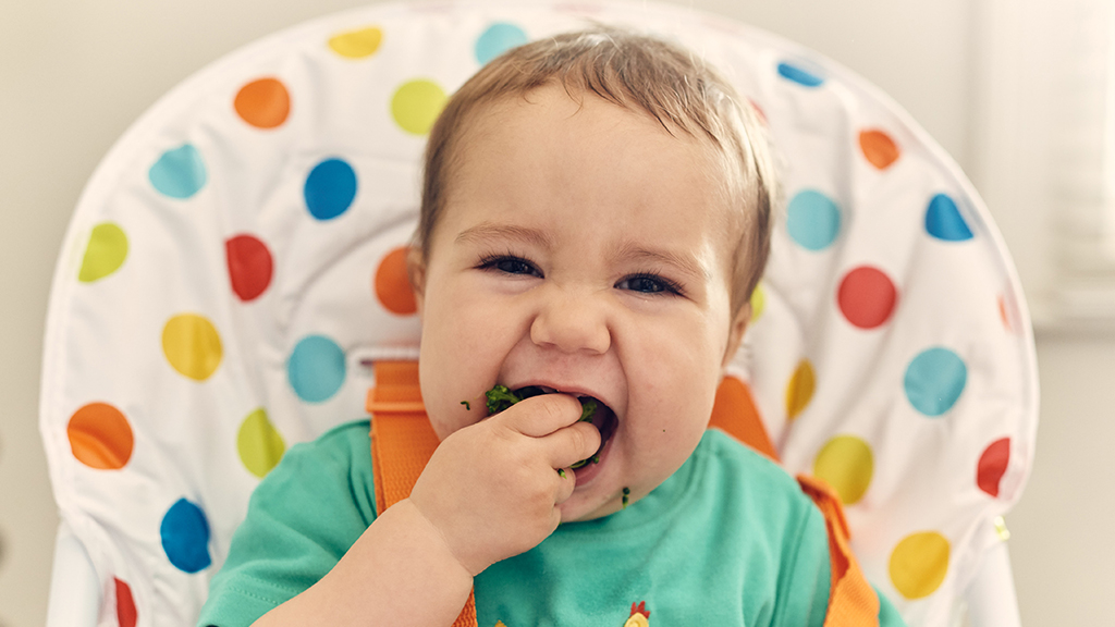 smiling baby eating broccoli